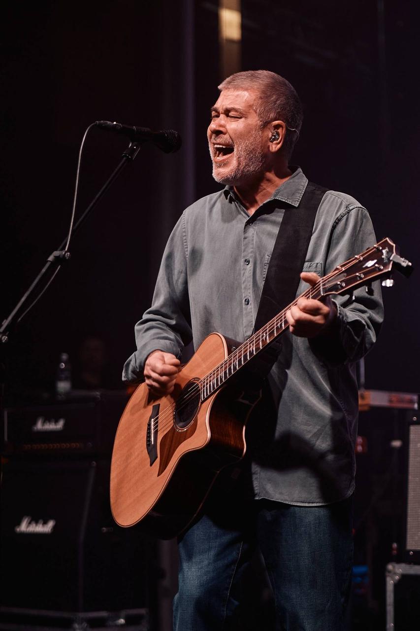 A musician playing an acoustic guitar on a red-lit stage