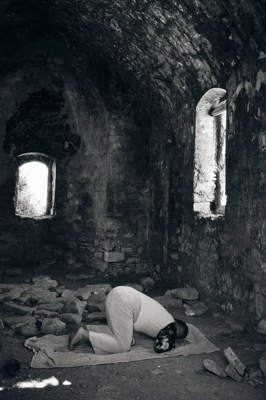 A person crouching in a dark vaulted passage lit by a window