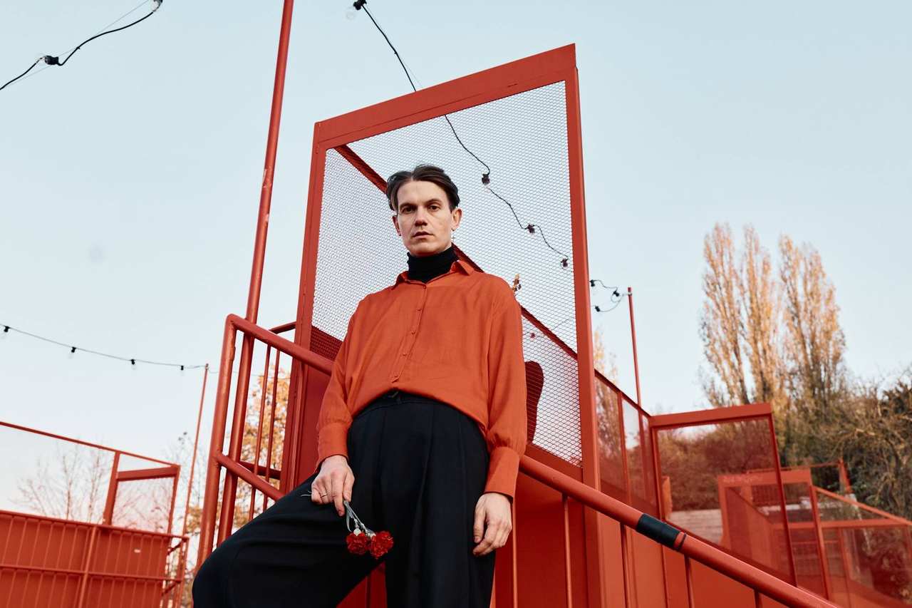 A model in a red coat standing on a red steel bridge